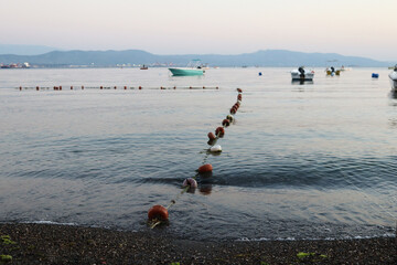 Calm seaside with fishing boats and floating buoys along a rocky beach © Альфира Зиганшина