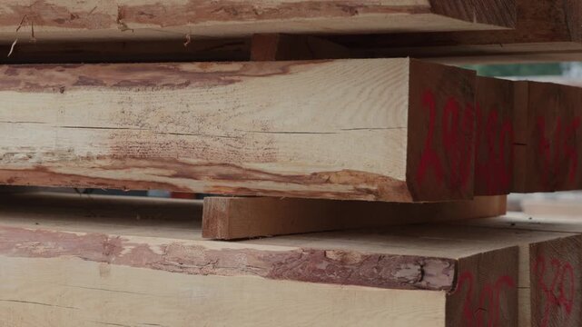 Forklift operator moving large rough-sawn timber beams in an outdoor lumber yard, illustrating heavy material handling, storage, and wood industry logistics