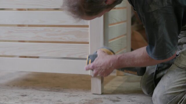 Carpenter using an orbital sander to smooth a wooden frame in a woodworking shop, showing hands-on craftsmanship and furniture finishing