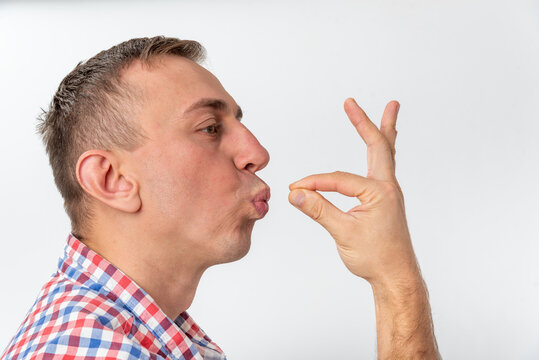 Young man creating a fun hand puppet animal illusion with his fingers, puckering his lips as if kissing or feeding the imaginary creature, standing against a clean white background