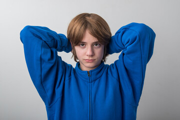 Young person looking directly at the viewer with a neutral expression while wearing a blue fleece jacket and resting hands behind their head, portraying casual comfort and relaxed posture © somemeans