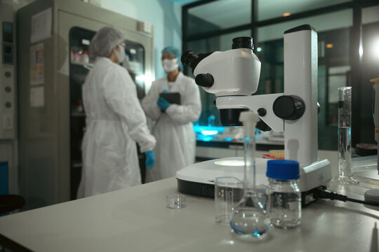 Scientists in Lab Coats Discussing Quality Control Results Near Stereo Microscope in Pharmaceutical Research Laboratory