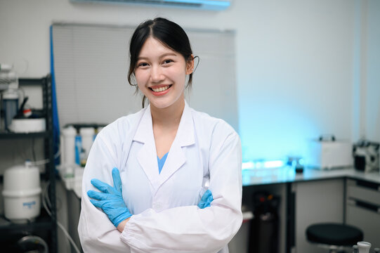 Young Asian Female Scientist Smiling Confidently in Laboratory Wearing White Lab Coat and Blue Gloves