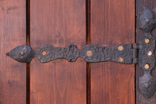 Ornate dark metal hinge securing a weathered brown wooden door, showcasing handcrafted hardware and traditional craftsmanship, reflecting history and vintage style