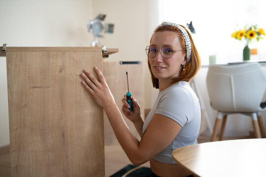 A white woman is assembling wooden furniture