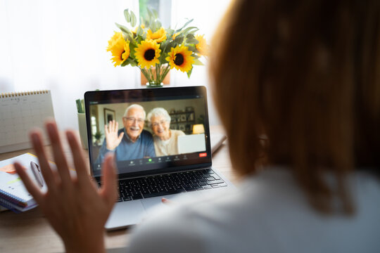A white woman waves at a senior couple during a video call at home
