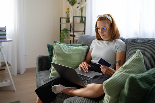 A white woman shops online at home using a laptop and a credit card
