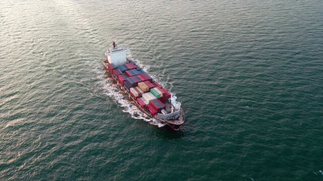 A container cargo vessel sails on open ocean, carrying stacked colorful shipping containers for maritime transport.
