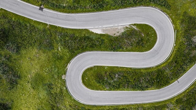 Aerial view of the winding hairpin turns of the Pordoi Pass road surrounded by lush green mountain slopes in Canazei, Trentino-Alto Adige, Italy.