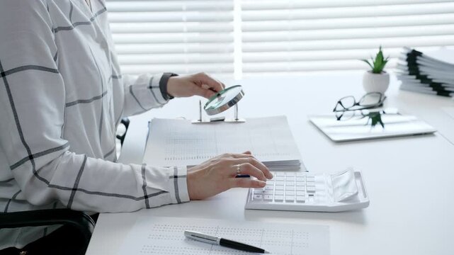Financial professional carefully reviewing business documents with a magnifying glass while calculating numerical data, demonstrating diligent tax preparation and detailed audit analysis