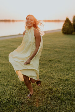 Woman runs in a yellow dress near water at sunset in a grassy area