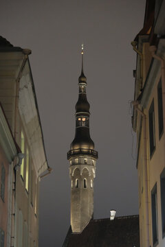 framed view of Tallinn Town Hall tower spire between historic alley buildings at night.