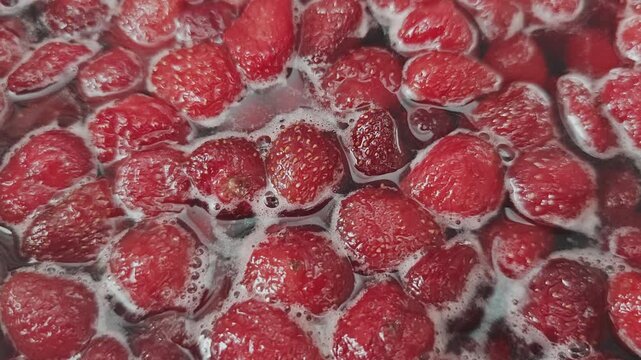 Close up of fresh strawberries boiling in sugar syrup. Preparation process of homemade berry jam, marmalade, or confiture in a saucepan