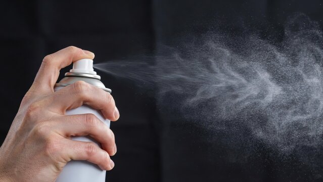 Hand with spray can and mist on dark background