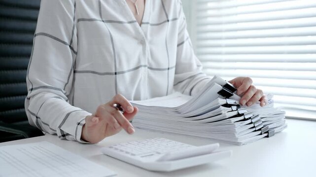 Accountant or financial professional reviewing business documents and calculating expenses on a white desk, managing taxes, financial records, and official paperwork for audit or reporting