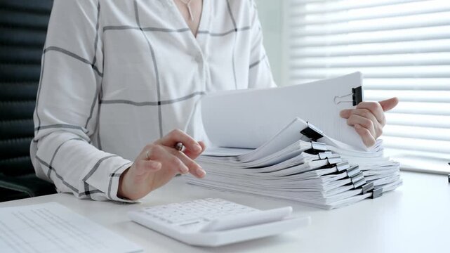 Accountant or financial professional reviewing business documents and calculating expenses on a white desk, managing taxes, financial records, and official paperwork for audit or reporting