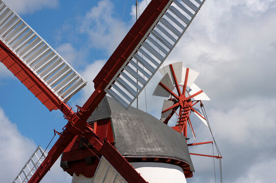 Traditional red and white windmill with large wooden sails against blue sky and clouds