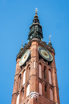 The historic brick clock tower of the Main Town Hall rises into the sky in the old town of Gdansk, Poland, displaying intricate architectural details.