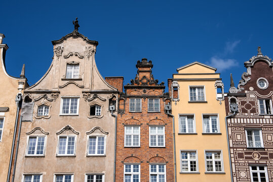 Ornate historic tenement house facades stand side by side under a clear sky in the old town of Gdansk, Poland, displaying traditional architectural details.