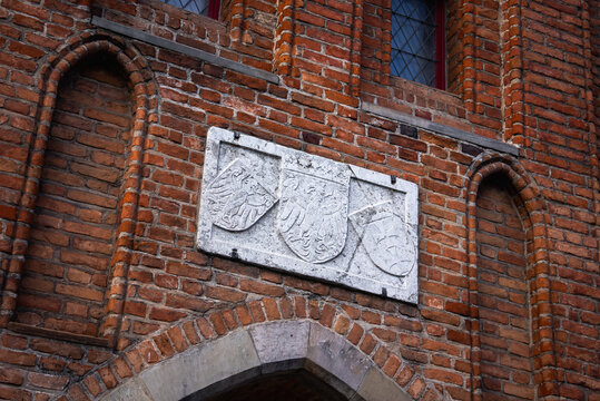 An ancient stone carved coat of arms plaque mounted on the historic gothic red brick facade of a heritage structure in the old town of Gdansk, Poland.
