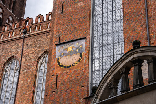 A detailed view of the exterior brick wall, Gothic tall windows, and painted sundial on Saint Mary Church in the historical old town of Gdansk, Poland.