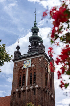 The historic brick tower and ornate spire of Saint Catherine Church rise beneath a cloudy sky in the old town of Gdansk, Poland.