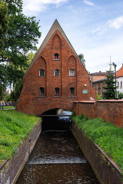 Historic brick facade of the Small Mill built over the flowing water canal of Radunia river in old town Gdansk, Poland under a clear sky.