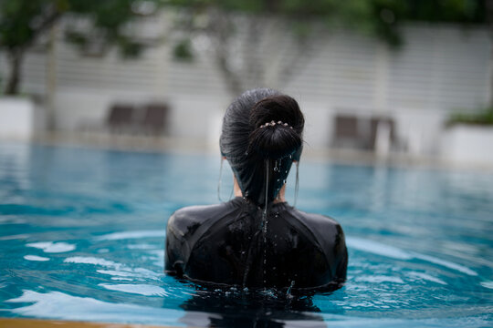 Rear view of Asian woman in black swimsuit relaxing in swimming pool