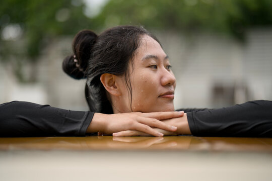 Smiling Asian woman resting on the edge of a swimming pool