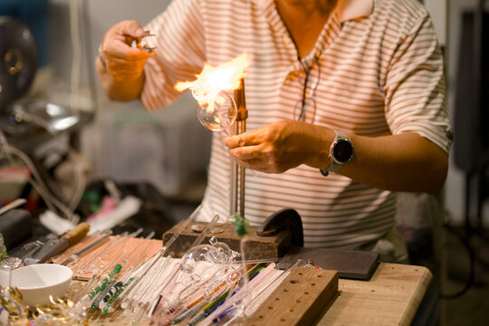 Artisan shaping molten glass with a torch flame in a workshop