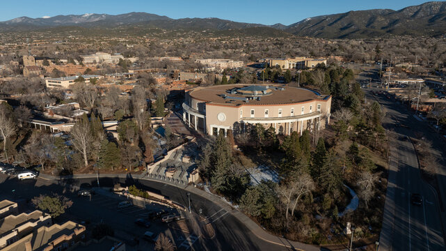 Aerial view of the New Mexico State Capitol, also known as the Roundhouse, surrounded by trees and urban infrastructure in Santa Fe, New Mexico, United States.
