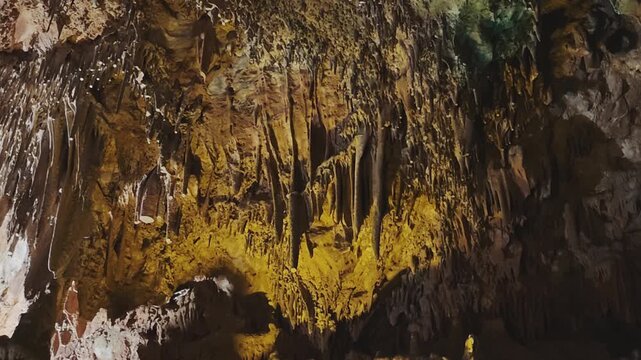 Majestic cavern with impressive rock formations, stalactites, and stalagmites illuminated by artificial yellow lights creating a mystery atmosphere