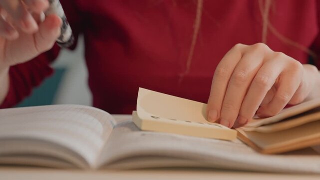 Woman in red top writes on sticky notes. Woman places cards labeled bread near books flipping. Close up view emphasizes hands performing tasks like writing upside down