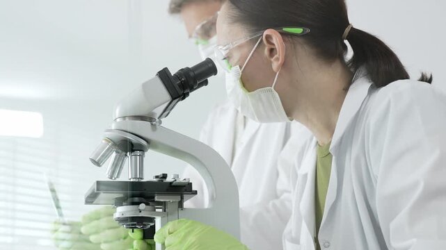 Researchers actively performing scientific analysis in a laboratory. Looking through a microscope to examine biological samples. Focusing on discovery. Innovation