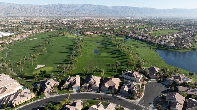 Aerial view of a lush green golf course surrounded by residential homes, palm trees, and a small lake in Indio, California, United States.