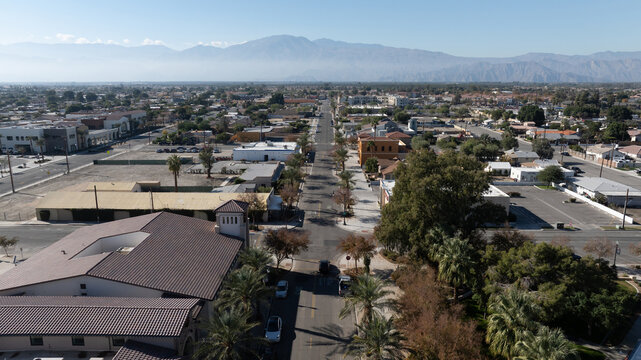 Aerial view of the town of Coachella featuring palm trees, low-rise buildings, and distant mountains under a clear sky in Coachella, California, United States.