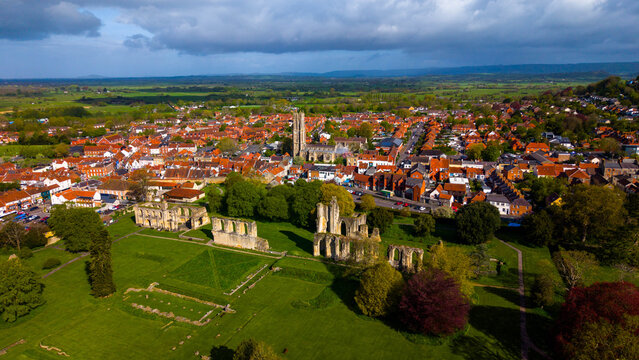 Aerial view of the historic ruins of Glastonbury Abbey surrounded by green lawns, with the town of Glastonbury and its red-tiled rooftops in Glastonbury, England, United Kingdom.