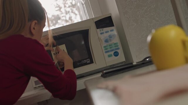 Young woman in red shirt places and adjusts food labeled bread. Woman interacts closely with oven ensuring proper placement. Scene is set indoors on counter next to open door