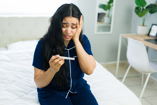 Stressed woman in pajamas finding a negative pregnancy test result, feeling worried in her bedroom