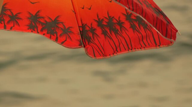 Beach umbrella, ocean, water. Red beach umbrella with palm tree pattern on a sunny day with sparkling ocean background.