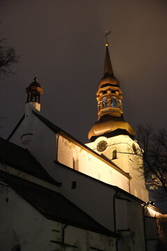 Low-angle view of the illuminated facade and baroque clock tower spire of Tallinn St Mary's Cathedral at night.