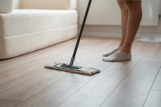 A person mops the wooden floor with a cleaning tool while wearing socks in a living room