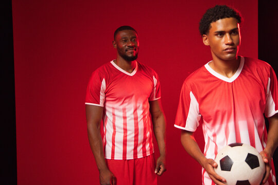African American men standing in red studio wearing red-and-white jerseys and holding soccer ball