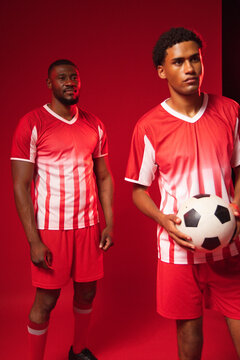 African male teammates standing in studio wearing red white jerseys holding black white soccer ball