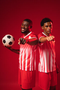 African American men posing in studio wearing red striped jerseys, pointing and holding soccer ball
