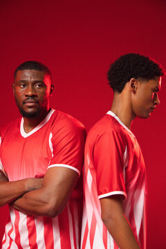 Two African male teammates standing back-to-back against red studio backdrop wearing matching kits