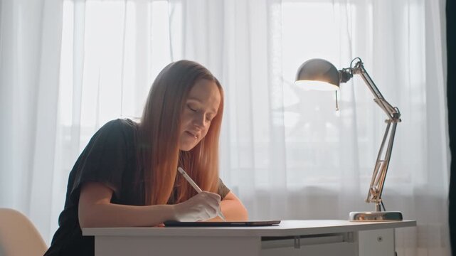 Young woman with long hair is seated at white desk interacting steadily. Woman maintains focus. Scene emphasizes her continuous engagement in digital drawing showing woman