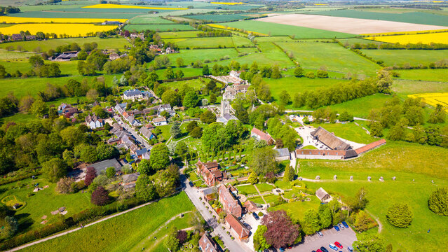 Aerial view of Avebury Stone Circle, a Neolithic henge monument, surrounded by the historic village of Avebury, green fields, and yellow crops in Avebury, Wiltshire, United Kingdom.