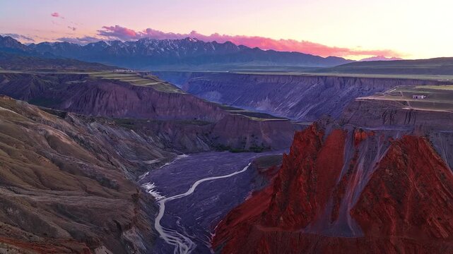 Aerial view of a deep gorge with a winding river and red cliffs at sunset in Anjihai Grand Canyon, Xinjiang, China
