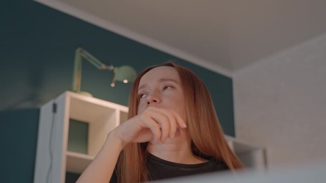 Young woman with long straight hair engages. Woman rests on one hand at times while maintaining focus downward. Scene is indoors with consistent lighting and background elements
